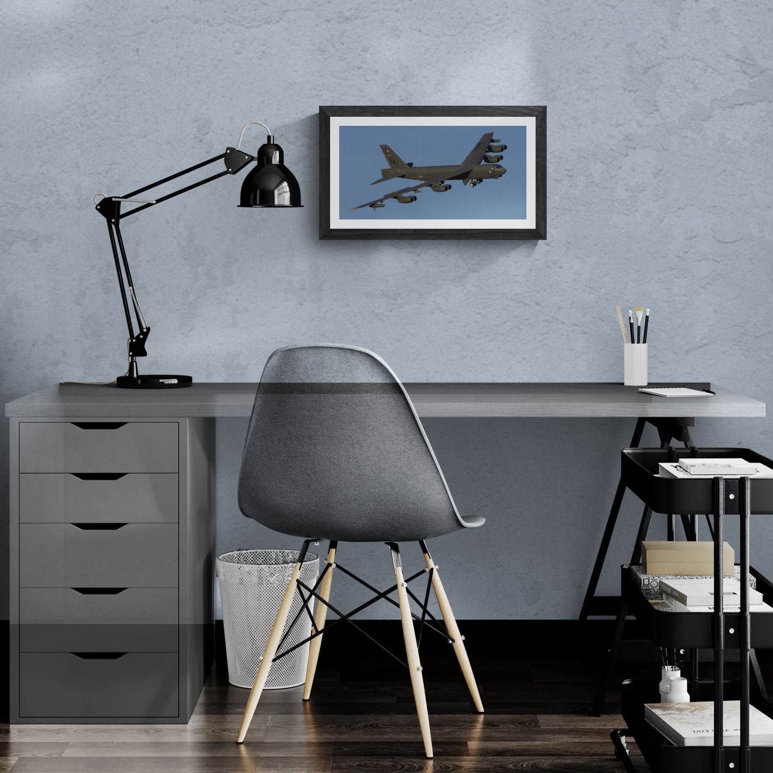A 20x10 "Standard Edition" of the "B-52 Stratofortress: The Industrial Titan" print featured in a modern home office. The textured black gallery frame is mounted on a light-blue textured wall above a white desk, illustrating the panoramic scale and industrial detail of the B-52 in a personal workspace.