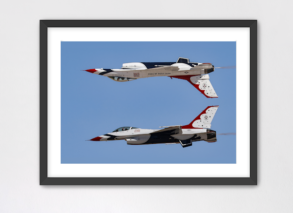 Fine art print of the Thunderbirds Calypso Pass maneuver. The photo captures the #5 F-16 flying upside down directly above the #6 jet against a clear blue sky, presented in a black gallery frame with a white mat.