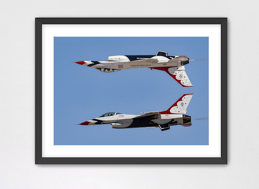 Fine art print of the Thunderbirds Calypso Pass maneuver. The photo captures the #5 F-16 flying upside down directly above the #6 jet against a clear blue sky, presented in a black gallery frame with a white mat.