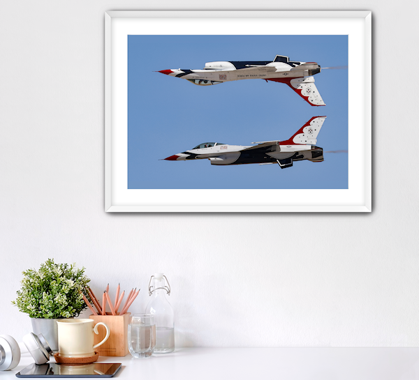 Framed photography print of the USAF Thunderbirds performing the Calypso Pass, hanging above a desk in a bright, modern office. The image shows two F-16 jets, one inverted over the other.