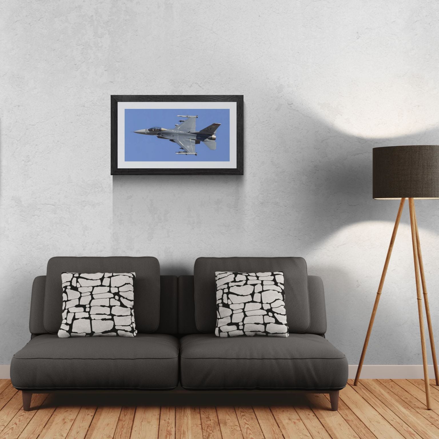 A 30x15 'Gallery Edition' of the 'Viper Launch' F-16 aviation print. The textured black gallery frame anchors the matted print on a light-textured wall above a modern dark gray sofa. To the right, a tripod floor lamp provides a residential scale reference for this /50 limited edition deployment, showcasing the airframe’s technical detail and scale for a primary living space.