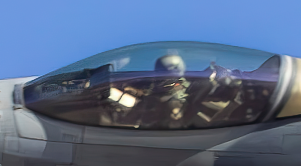 Extreme close-up detail of an F-16 cockpit showing the pilot in a helmet and the reflections on the canopy. This high-resolution macro shot highlights the sharpness of the metallic fine art paper used by photographer Phil Schmauder.