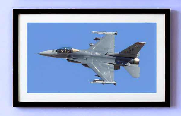 Framed limited edition print of a U.S. Air Force F-16 Viper departing Nellis Air Force Base. The photo is matted in white with a black frame, showing the aircraft banking with a full payload during Red Flag 25-1.