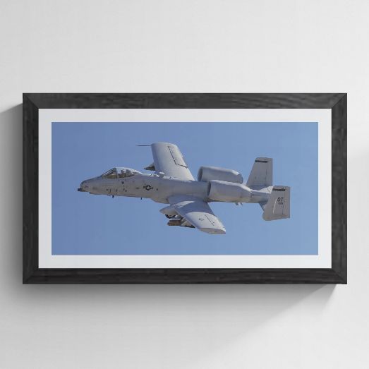 Limited edition A-10 Thunderbolt II photography print titled "Titanium and Grit" by Phil Schmauder at Nellis AFB. The panoramic master is professionally presented in a textured black gallery frame with a crisp white mat against a light gray background, highlighting the GAU-8 nose cannon and "OT" tail code detail.