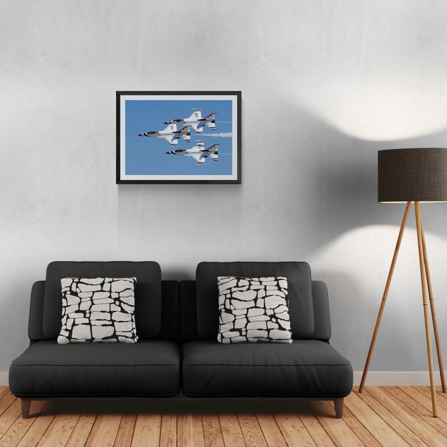 Gallery Edition size mockup of Triad Precision by PES Editions, showing the limited-edition Thunderbirds aviation art print framed and hanging in a modern living room setting over a dark grey sofa with geometric pillows next to a wood tripod floor lamp.