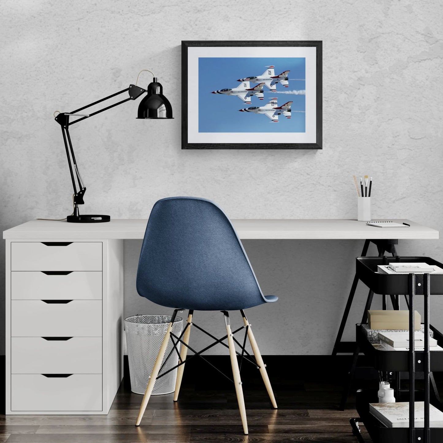 Standard Edition size preview of Triad Precision by PES Editions, displaying a framed military jet print as home office wall decor hanging above a modern white desk with a blue chair, black task lamp, and office organizers against a light textured wall.