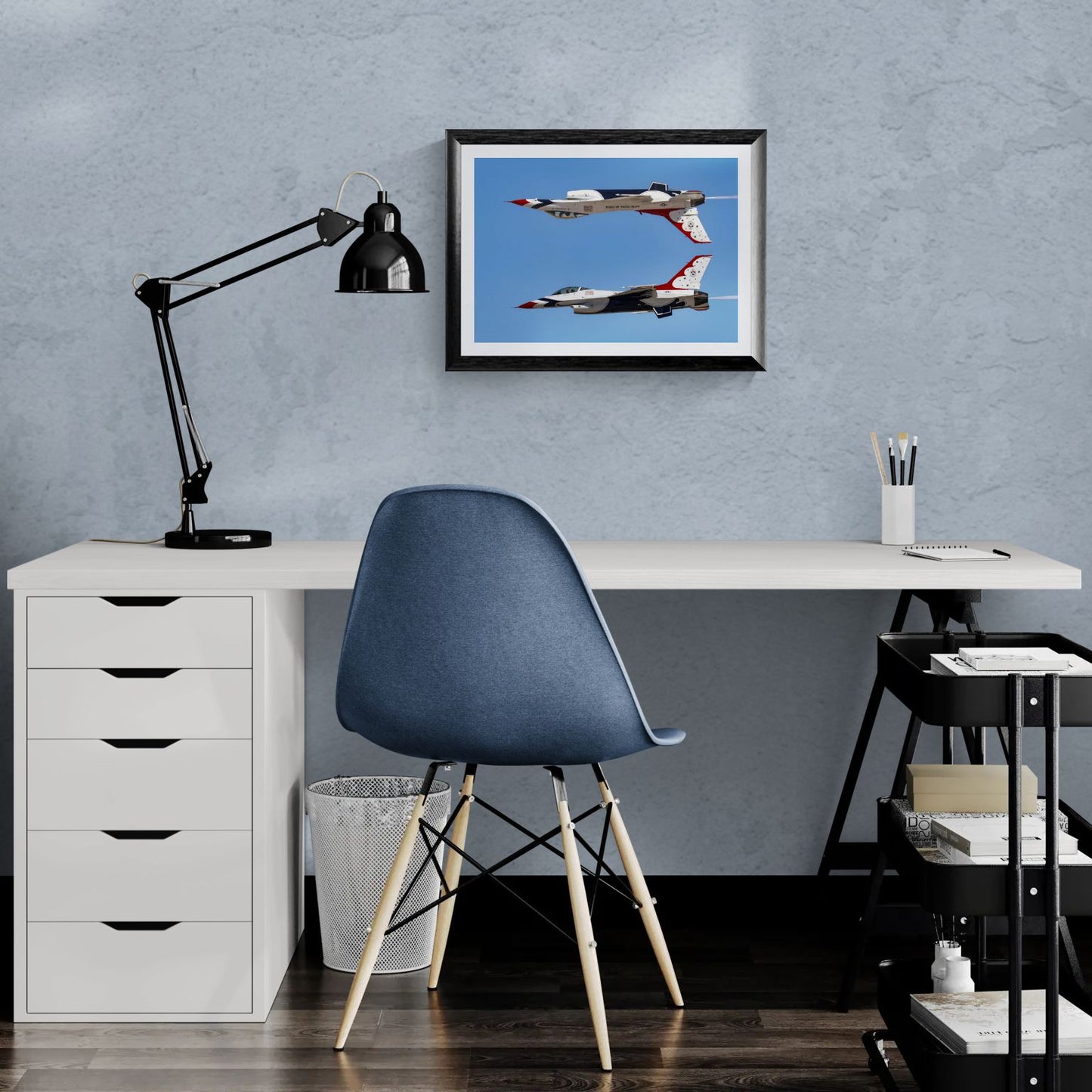 A 20x14 "Standard Edition" of the "Calypso Pass" Thunderbird print displayed in a modern home office setting. The textured black frame anchors a clean workspace featuring a white desk and a blue ergonomic chair, showcasing the print’s scale for personal galleries.