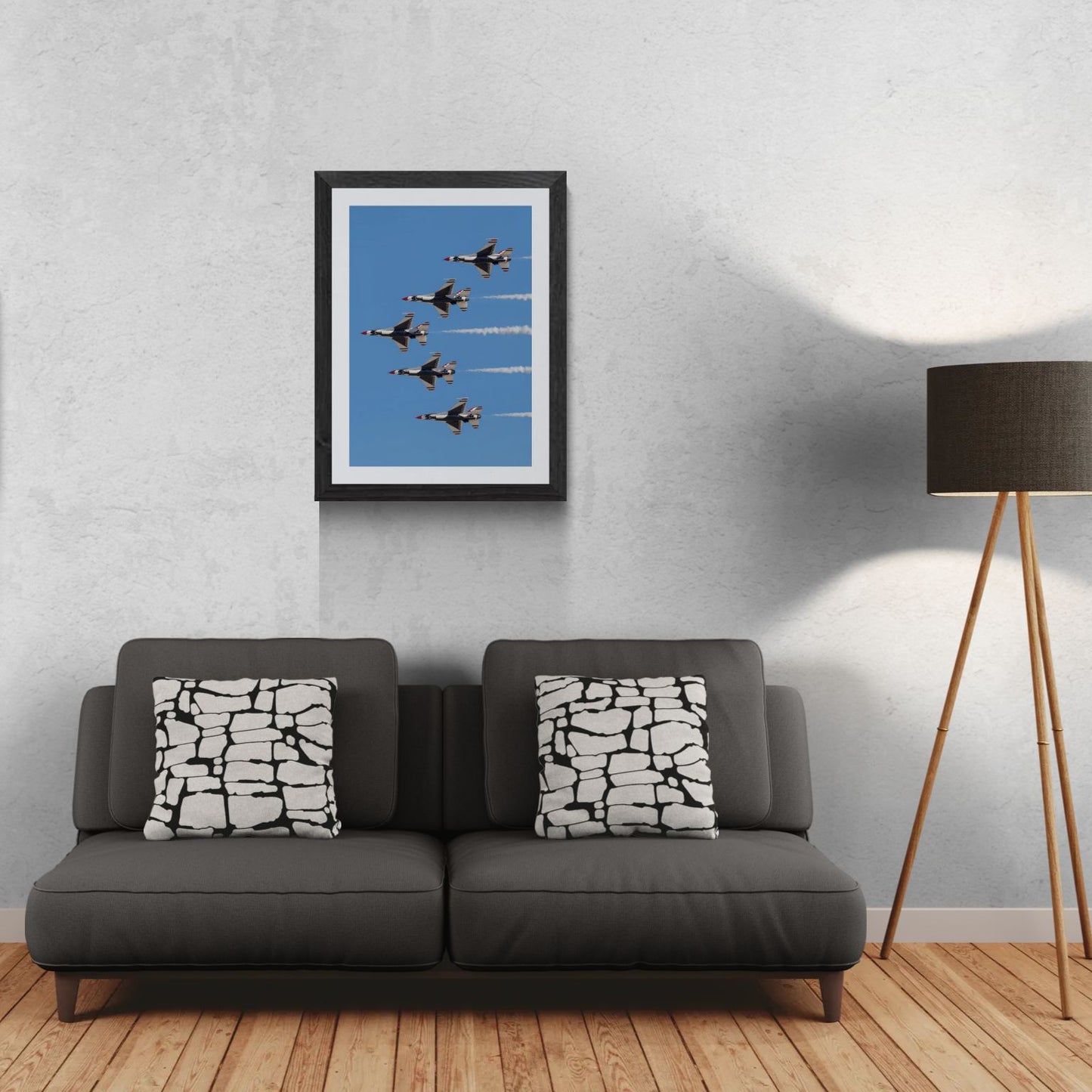 A 21x30 vertical Gallery Edition aviation photograph titled 'Delta Prime,' capturing the U.S. Air Force Thunderbirds in their iconic five-ship Delta formation during a vertical climb. The matted print is showcased in a sleek black gallery frame on a light-textured wall above a modern dark gray sofa. To the right, a tripod floor lamp provides a residential scale reference for this /50 limited edition deployment.