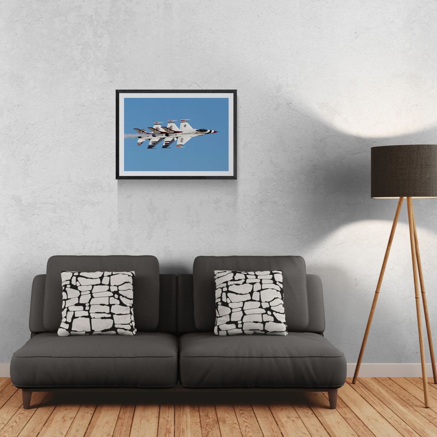 A 30x21 Gallery Edition aviation photograph titled 'Thunderbird Echelon Alpha,' featuring the U.S. Air Force Thunderbirds in a precise, tiered echelon formation against a clear blue sky. The matted print is housed in a sleek black gallery frame and displayed on a light-textured wall above a modern dark gray sofa. To the right, a tripod floor lamp provides a residential scale reference for this /50 limited edition deployment.