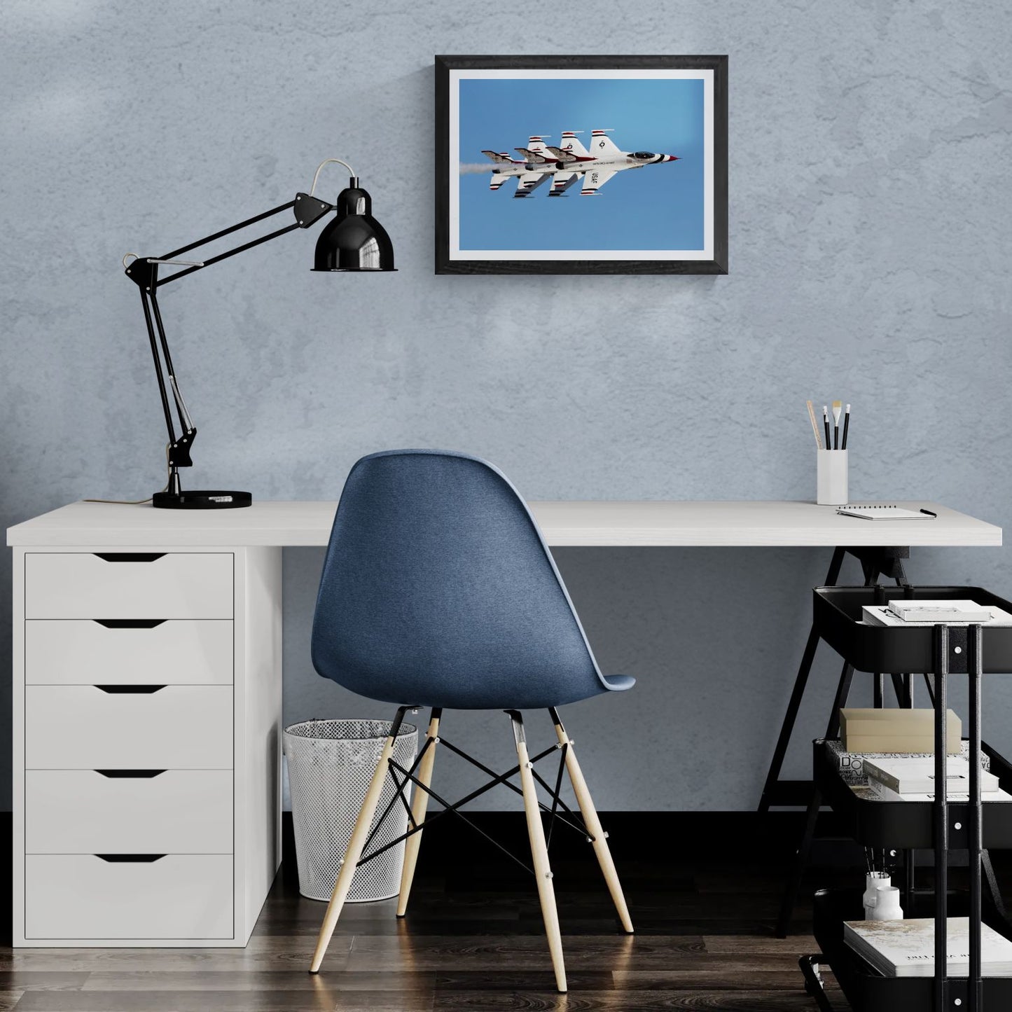 A 20x14 "Standard Edition" of the "Echelon Alpha" Thunderbird print displayed in a modern home office setting. The textured black gallery frame is mounted on a light-blue textured wall above a white desk, showcasing the print’s technical detail and scale for a personal workspace.