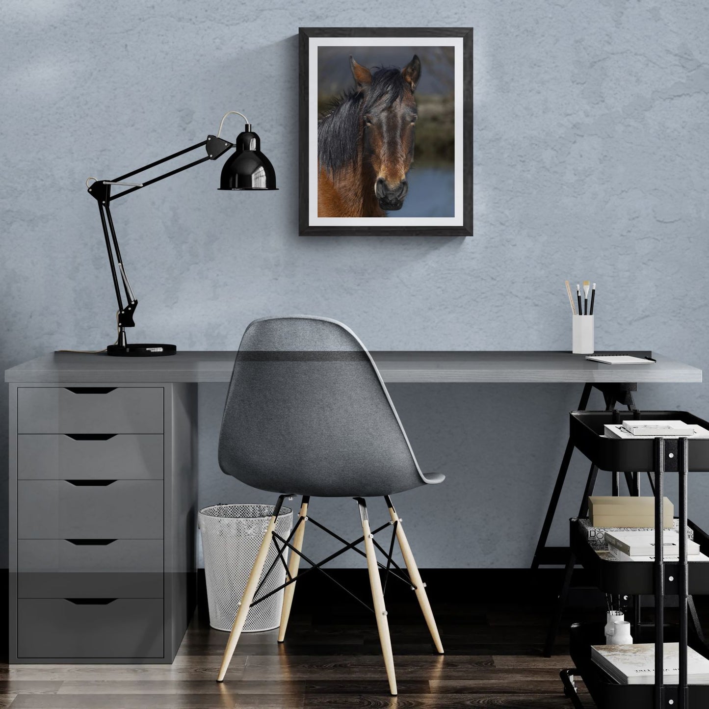 A 16x20 "Standard Edition" of the "Resilient Spirit" Wild Mustang print featured in a modern home office setting. The textured black gallery frame is mounted on a light-blue wall above a white desk, showcasing the print’s scale and organic detail for personal galleries.