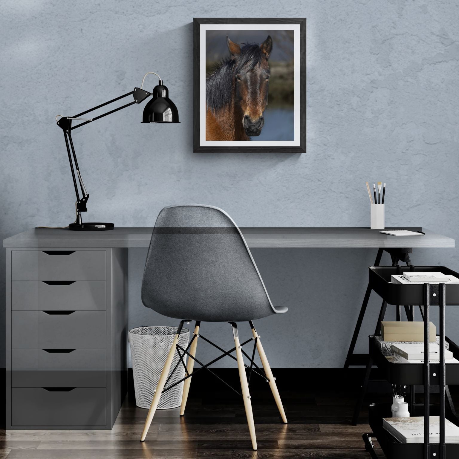 A 16x20 "Standard Edition" of the "Resilient Spirit" Wild Mustang print featured in a modern home office setting. The textured black gallery frame is mounted on a light-blue wall above a white desk, showcasing the print’s scale and organic detail for personal galleries.