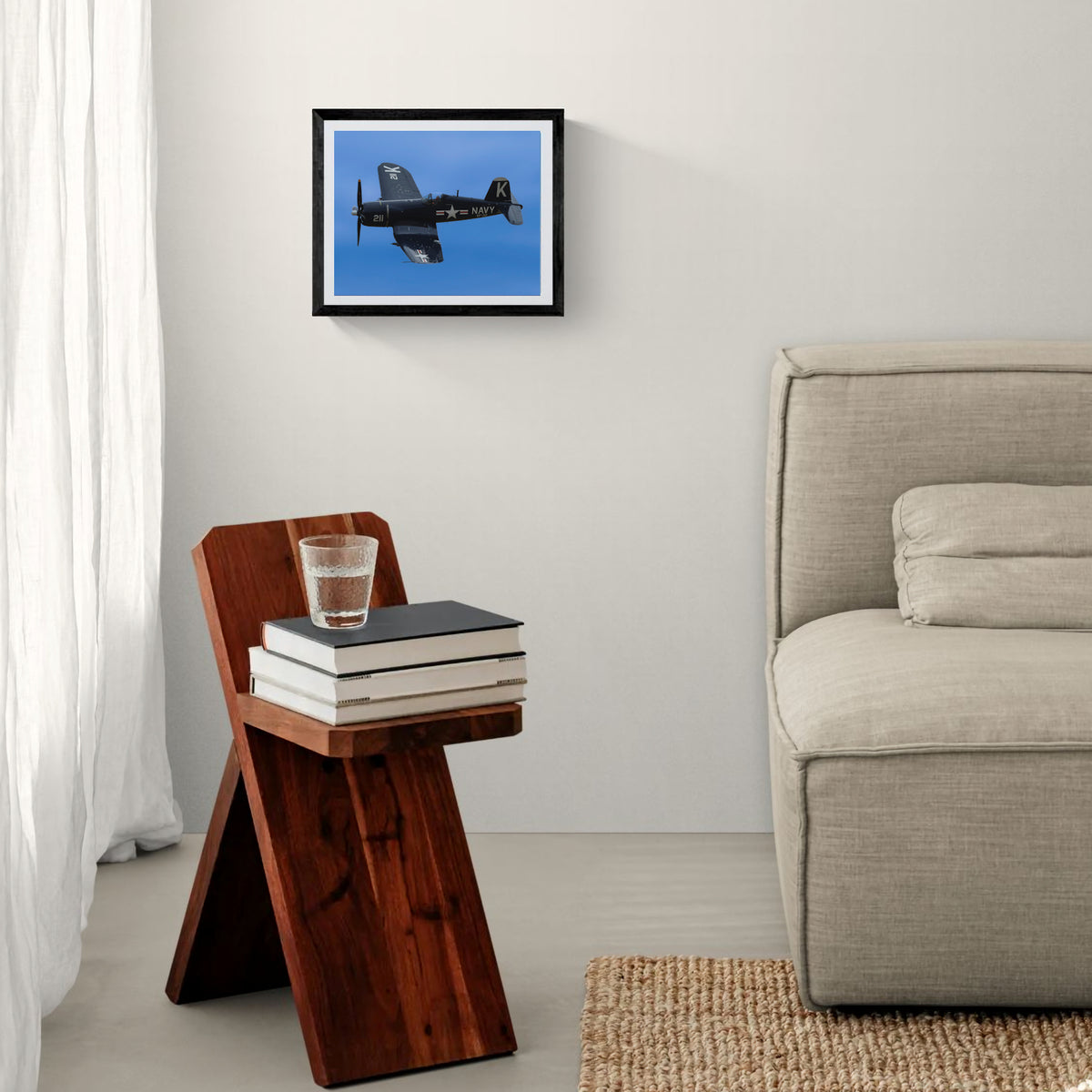 Bent Wing Bird F4U Corsair fine art print in a black frame mounted above a modern wooden side table next to a neutral fabric sofa.