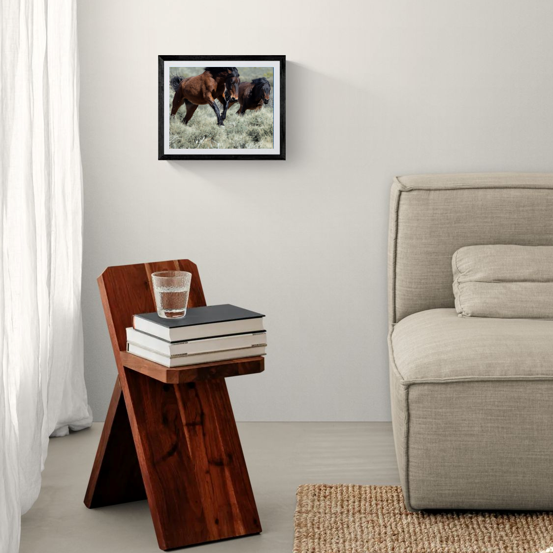 An 11x14 framed fine art wildlife print capturing running wild mustangs in the Nevada desert. The minimalist black frame hangs cleanly on a white accent wall over a rustic dark wood side table next to a neutral sofa.