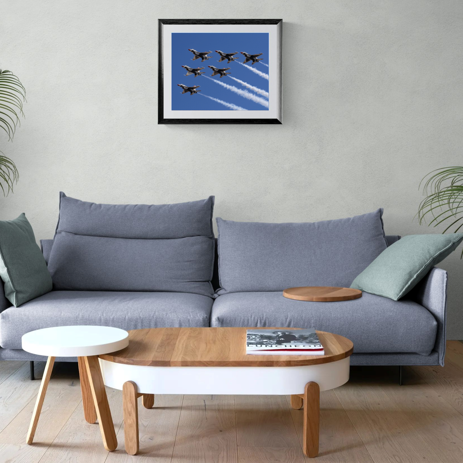 A large framed aviation print of the Thunderbirds diamond formation hanging on a textured gallery wall above a contemporary gray sofa and wooden coffee table in a bright living room.