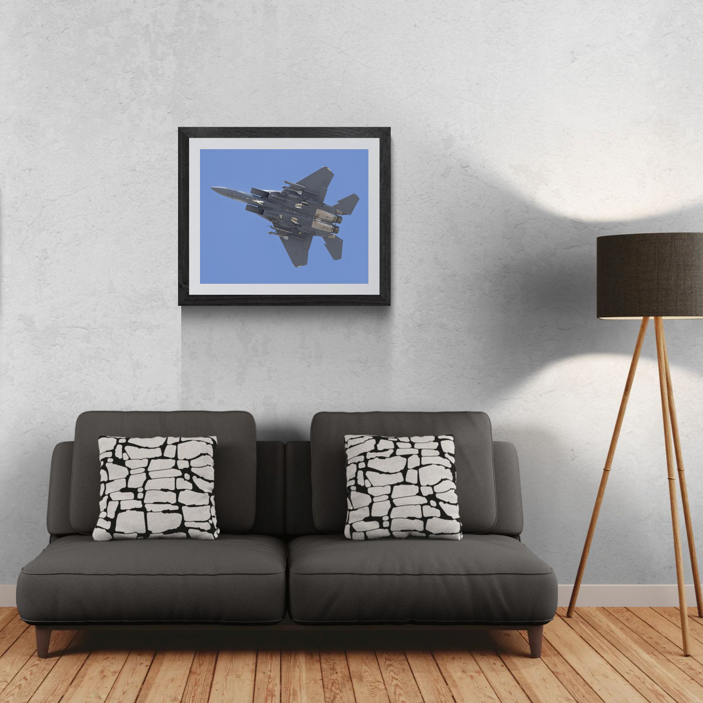Framed F-15 Strike Eagle jet wall art displayed above a grey sofa with patterned accent pillows in a modern living room setting.