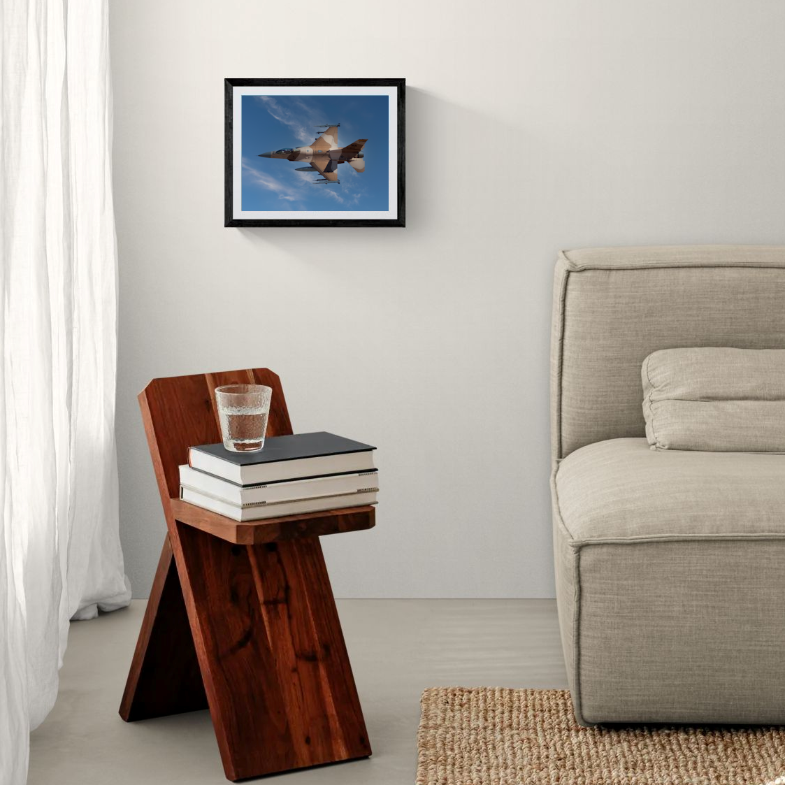 An 11x14 framed fine art print featuring a USAF F-16 Aggressor jet in flight. The minimalist black frame hangs on a crisp white wall above a dark wood accent side table next to a neutral-toned couch.