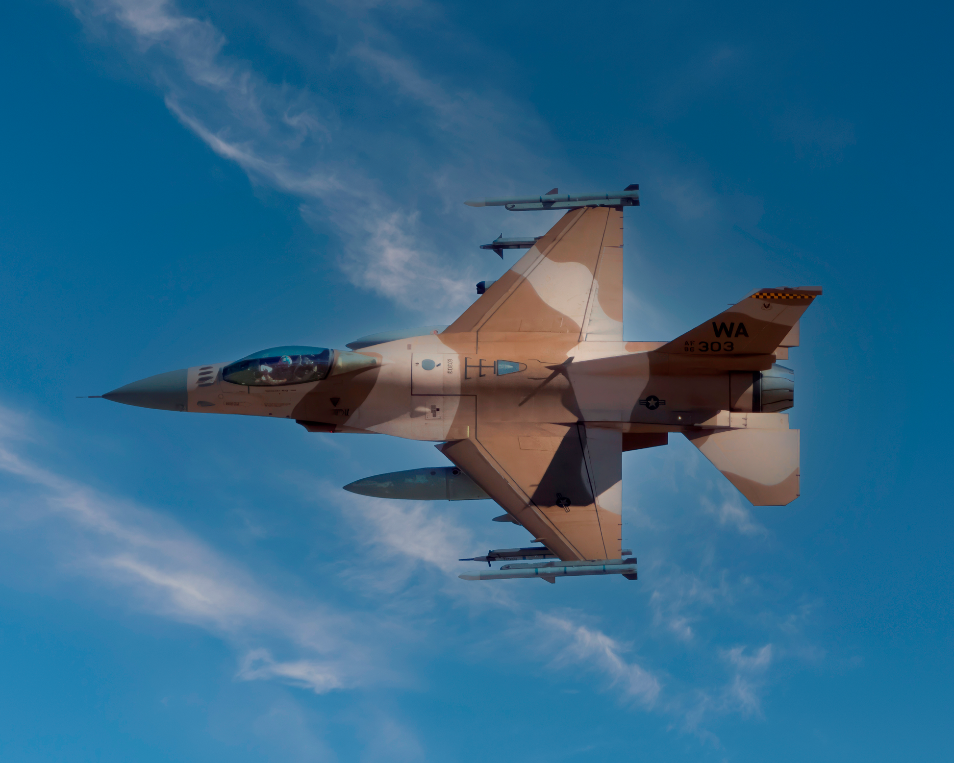 A sharp, full-bleed 10x8 fine art photograph of a USAF F-16 Aggressor fighter jet banking overhead against a deep blue sky with wispy, scattered clouds. The aircraft's distinct sand and brown desert camouflage scheme and tail code WA 303 are visible in exceptional technical detail.