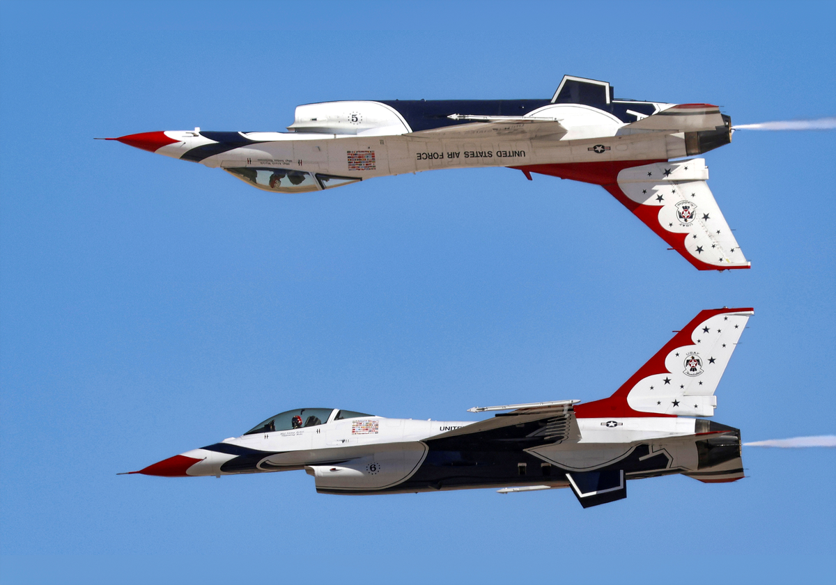 USAF Thunderbirds F-16 Fighting Falcons performing a Calypso Pass with Lead Solo inverted canopy-to-canopy over Opposing Solo against a clear blue sky.