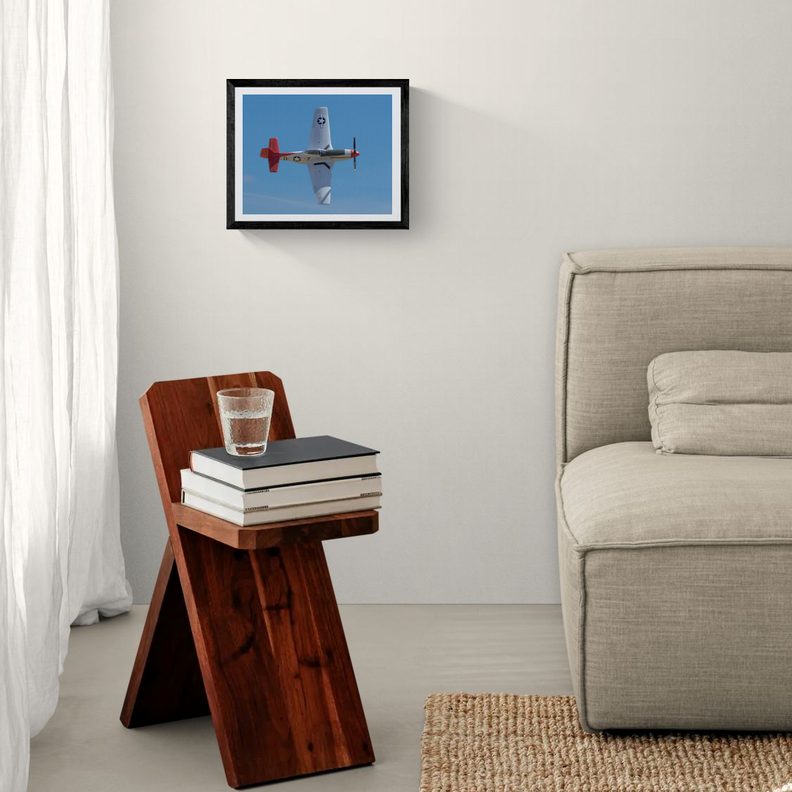 Framed P-51D Mustang fine art print in a black frame displayed on a minimalist white bedroom accent wall next to a modern wood side table.