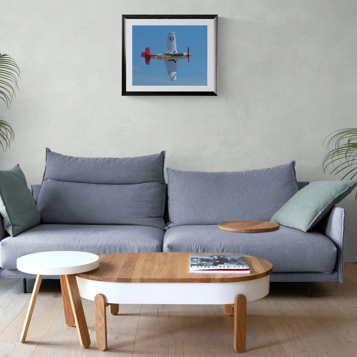 Framed fine art print of the P-51D Mustang Red Tail Sentinel centered above a contemporary gray sofa and modern wood coffee table.