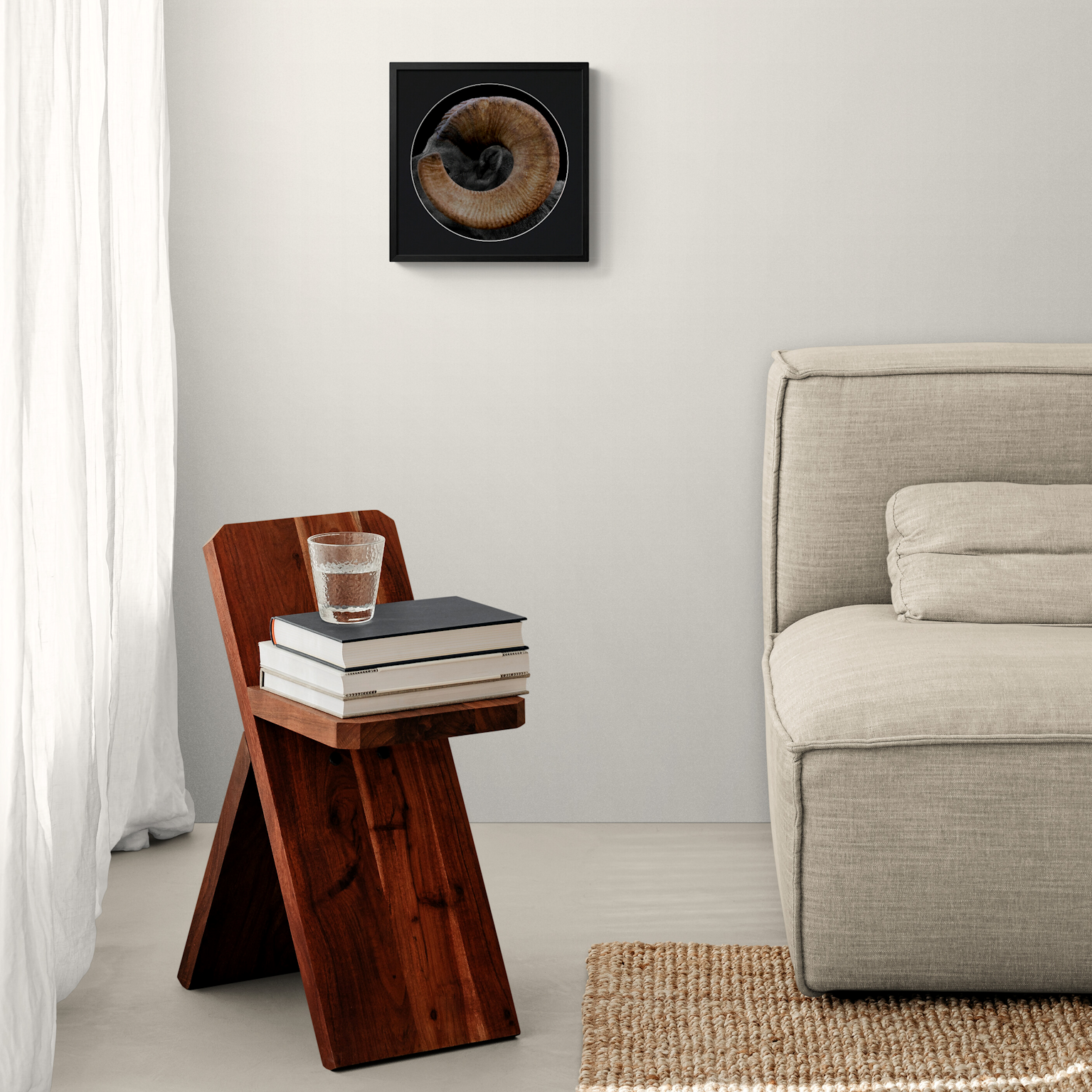 Square framed fine art print of a desert bighorn ram horn displayed on a light neutral wall above a rustic wooden side table and sofa.