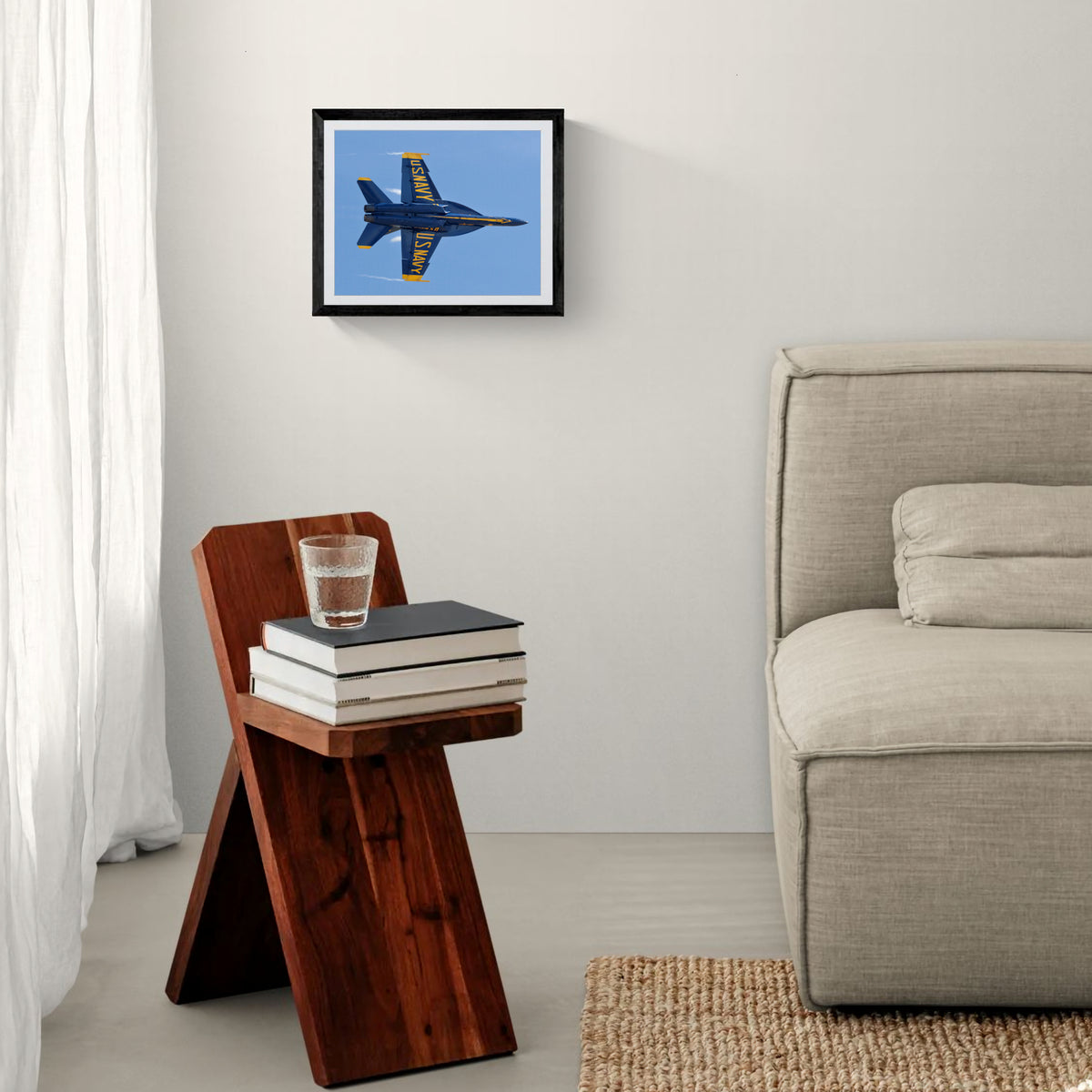 Framed Blue Angels F/A-18 fine art print mounted above a sculptural wooden side table and neutral upholstered armchair.