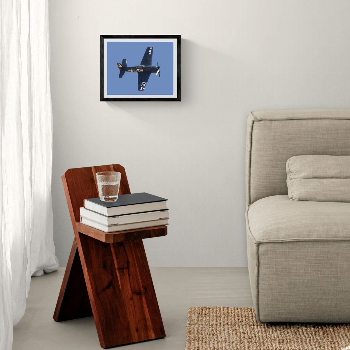 Framed The Final Cat F8F Bearcat aviation print hanging above a geometric wooden side table beside a fabric sofa.