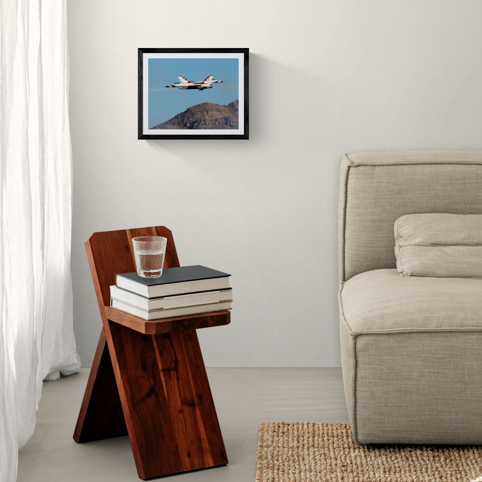 An 11x14 framed fine art print capturing the precision crossover flight of the United States Air Force Thunderbirds F-16 jets over a desert mountain ridge. The artwork is presented in a minimalist black frame hung on a clean white wall, situated above a rustic dark wood accent side table next to a neutral-toned sofa.